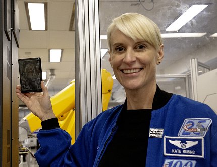 A smiling Rubins holds a dark gray, rectangular object with faint white markings.