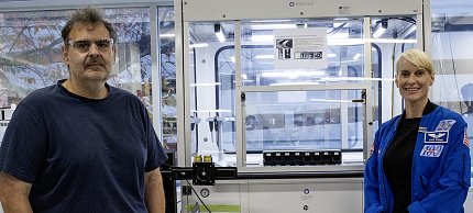 Rubins and a man in a dark t-shirt stand in front of a glass-fronted device.