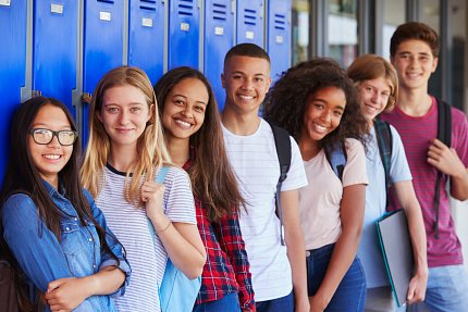 A row of smiling teenagers lean against blue school lockers.