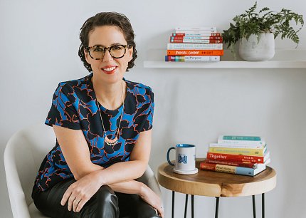 Amy Gallo smiling seated next to books, plant