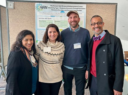 Four individuals pose in front of a scientific poster.