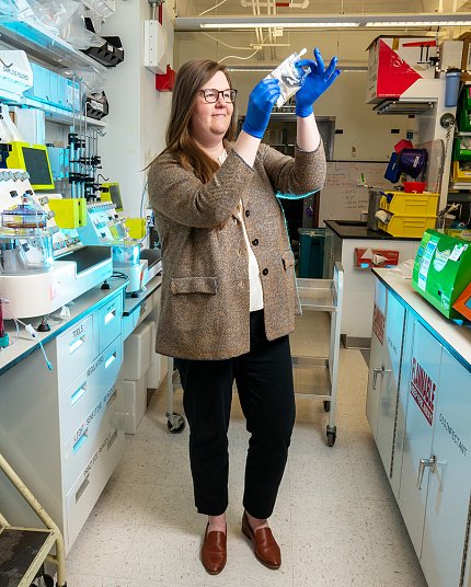 Song examines a sample. She is standing between two lab benches full of scientific instruments, and is wearing blue gloves.