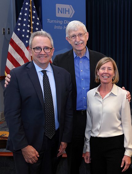 Burklow with Dr. Francis Collins and his wife with American flag behind