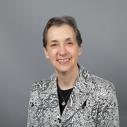 Headshot of Schor, who is smiling and wearing a black and white patterned jacket.