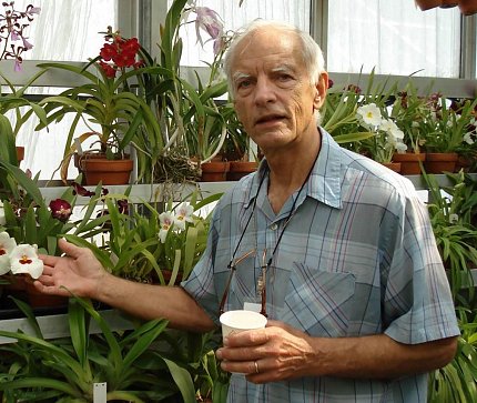 Brown, pictured in a greenhouse full of flowering plants, cups a white flower in his right hand. 