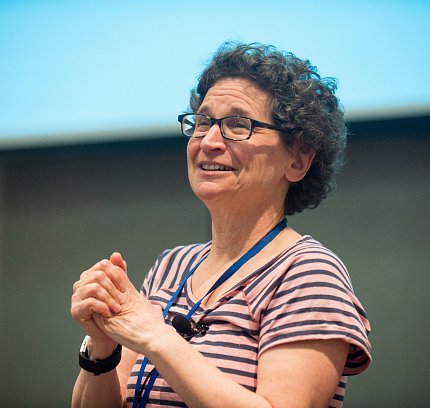 Milgram smiles as she speaks to a crowd in an auditorium.