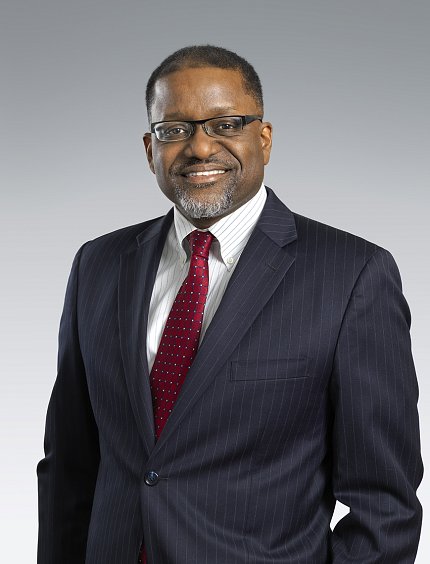 Professional headshot of Gibbons, who is smiling and wearing a suit and red tie.