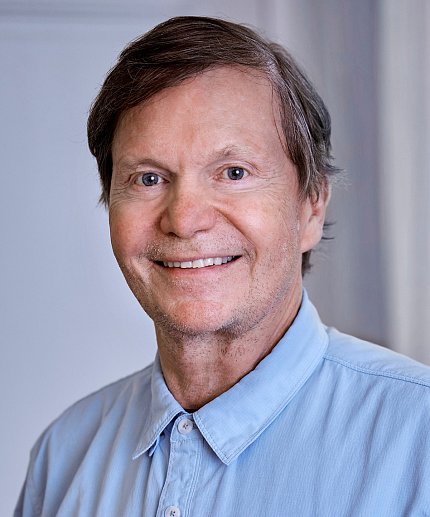 Headshot of Palsson, who is smiling and wearing a light blue button-up shirt