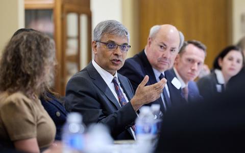 Bhattacharya speaks to a group while seated at table.