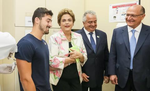 A clinical trial participant receives vaccine as former Brazilian president and other VIPs look on.