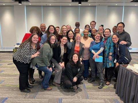 A large crowd poses for a photo in a carpeted conference room.