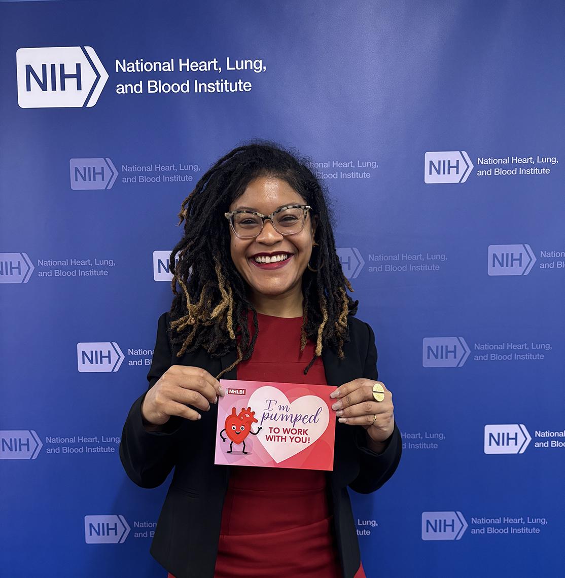 Brown smiling, wearing red, holding card with a heart