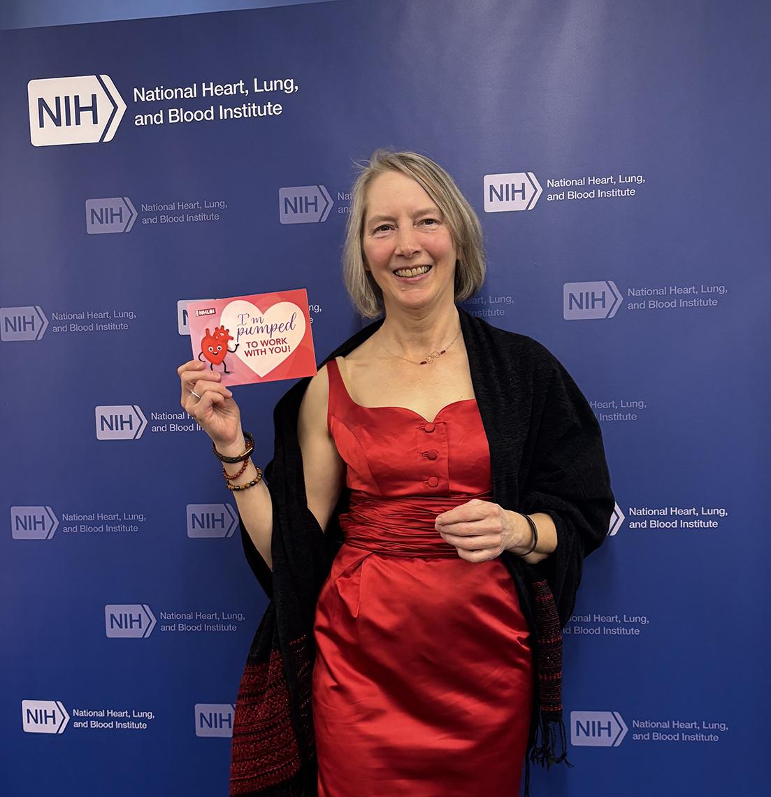 Jaquish in red dress holding card with heart-healthy pledge