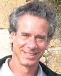 Headshot of Sacks in an outdoor setting. He has graying hair and is wearing a white shirt and black jacket.