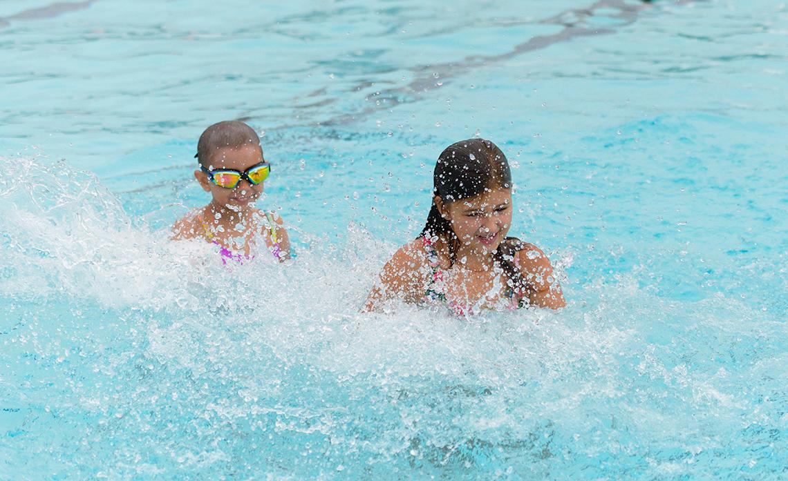 Two smiling kids splash in the swimming pool.