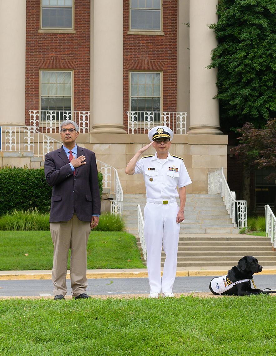 Bhattacharya observes the flag-raising with his hand over his heart. Wang salutes to his right.