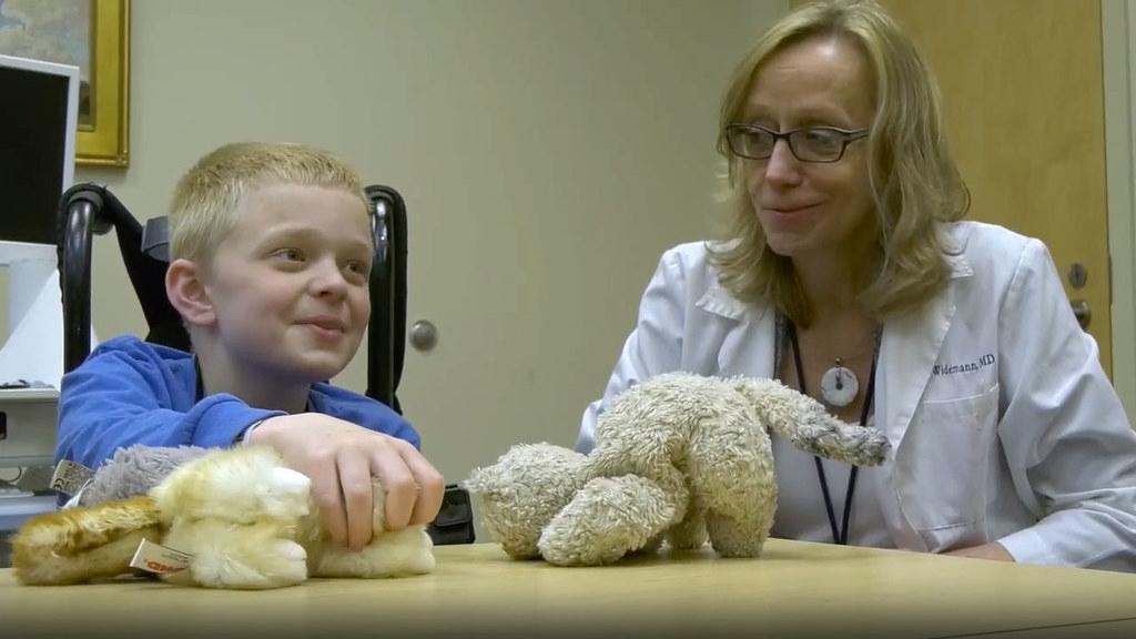 Widemann sits at a table with a young boy. The boy is playing with a stuffed animal.
