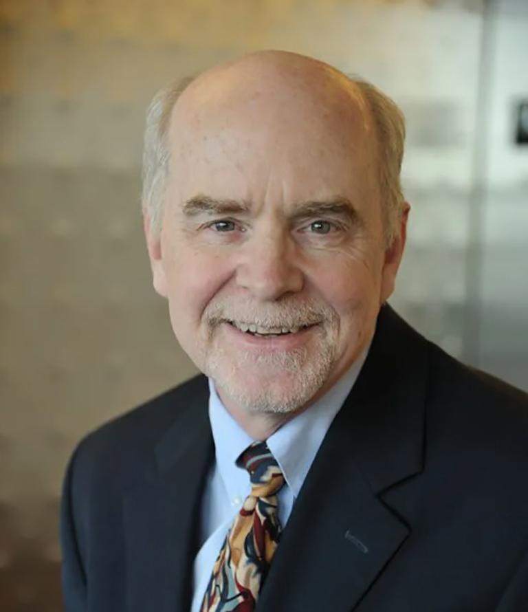 Headshot of O'Shea, who wears a suit and patterned tie.
