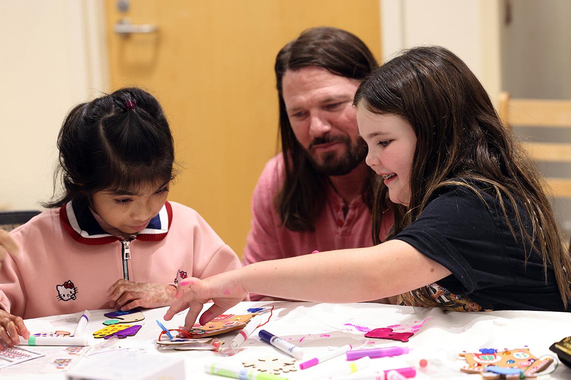 Wrestler sits smiling, watching two kids do crafts.