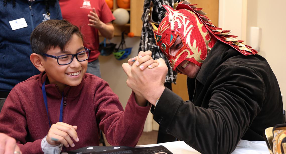 A smiling child arm-wrestles with Dragon Lee.