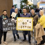 Group shot of colleagues standing together holding signs: Go Hector, Go NEI.