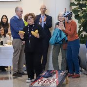 Zenk, smiling, holds beanbags in each hand, surrounded by cheering colleagues.