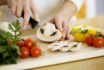 Vegetable prep close-up view of hands holding large mushroom being sliced with cherry tomatoes in foreground and half yellow bell pepper alongside