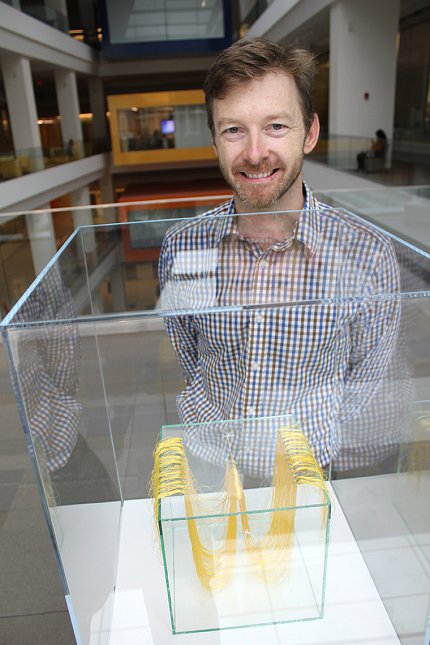 Conway neuroscientist artist Conway smiles, standing behind one of his exhibit pieces enclosed in a clear glass case..