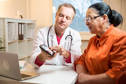 Doctor discusses test results with patient. A doctor shows a female patient her test results on an a tablet screen.