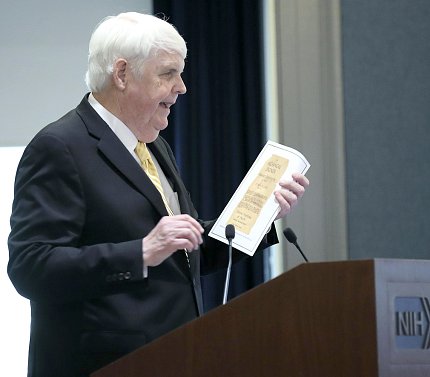 Clifford displays want ad At the podium, Clifford holds up clipping of the want ad he answered to work at NIH.