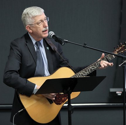 Dr. Francis Collins Collins holds guitar, sings into microphone