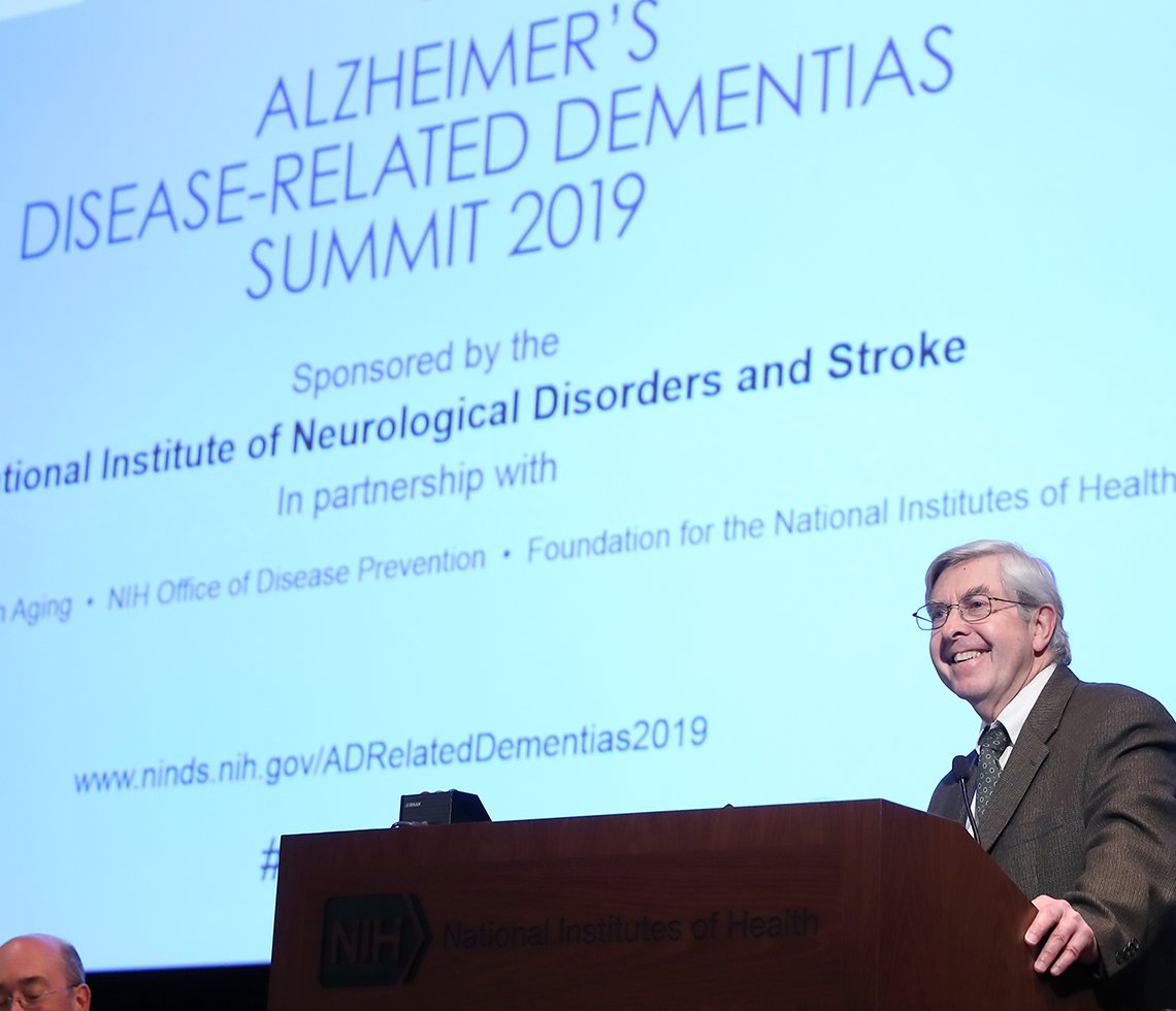 NINDS director Dr. Walter Koroshetz Dr. Koroshetz speaks in front of a screen.